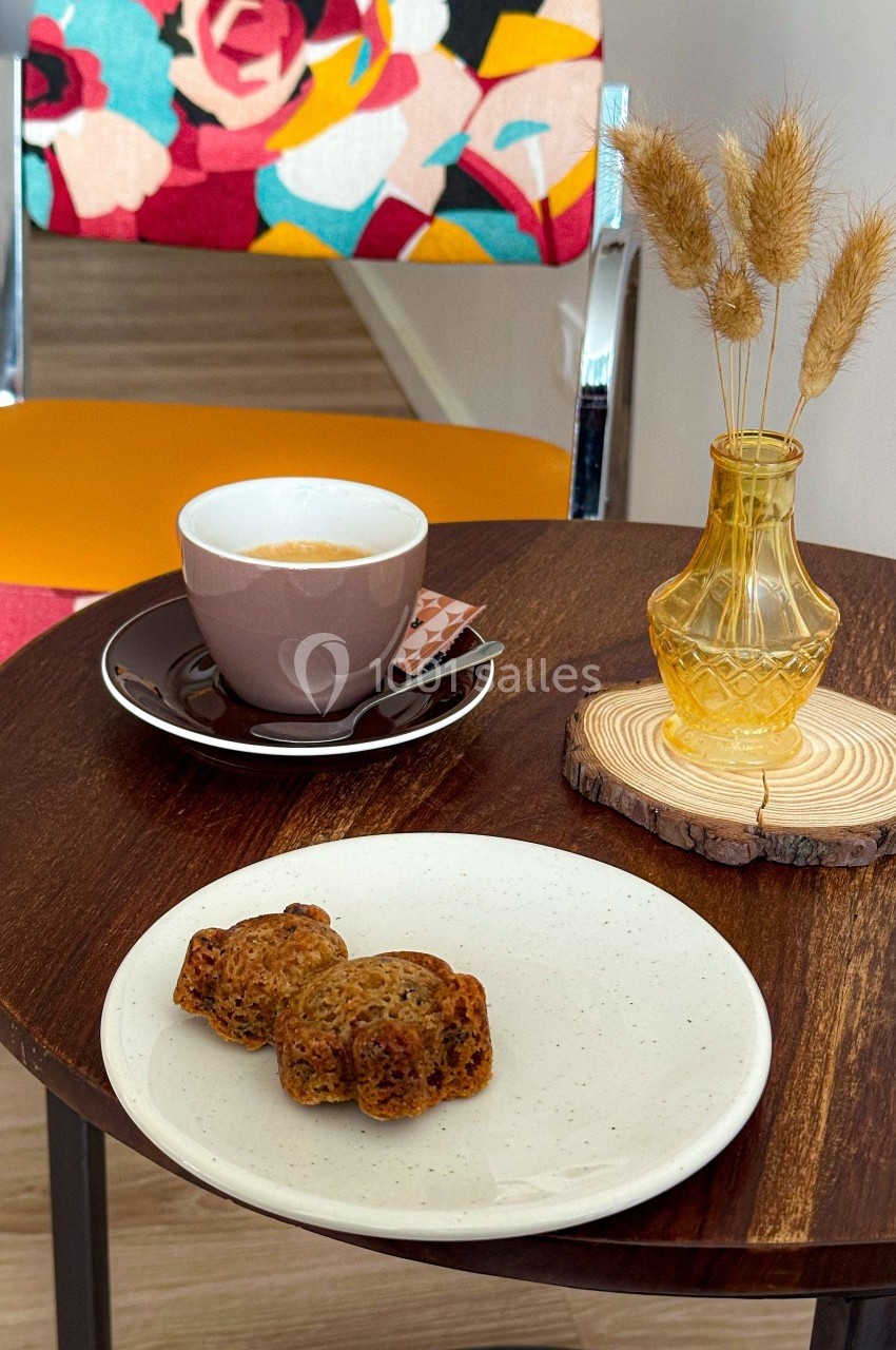 Tasse de café avec une assiette de petits gâteaux sur une table en bois, décorée d'un vase et d'une chaise colorée en…