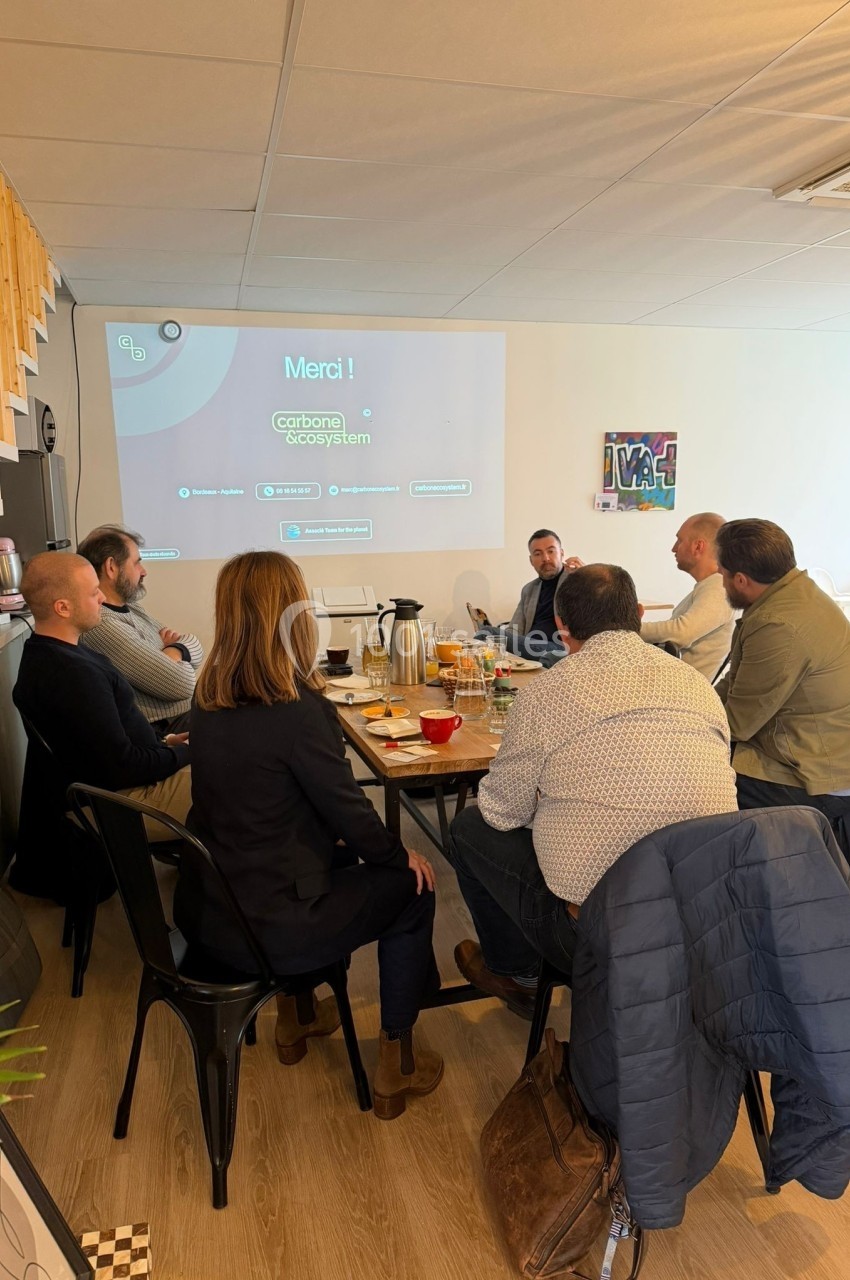 Un groupe de personnes assises autour d'une table en réunion dans une salle équipée d'un projecteur.