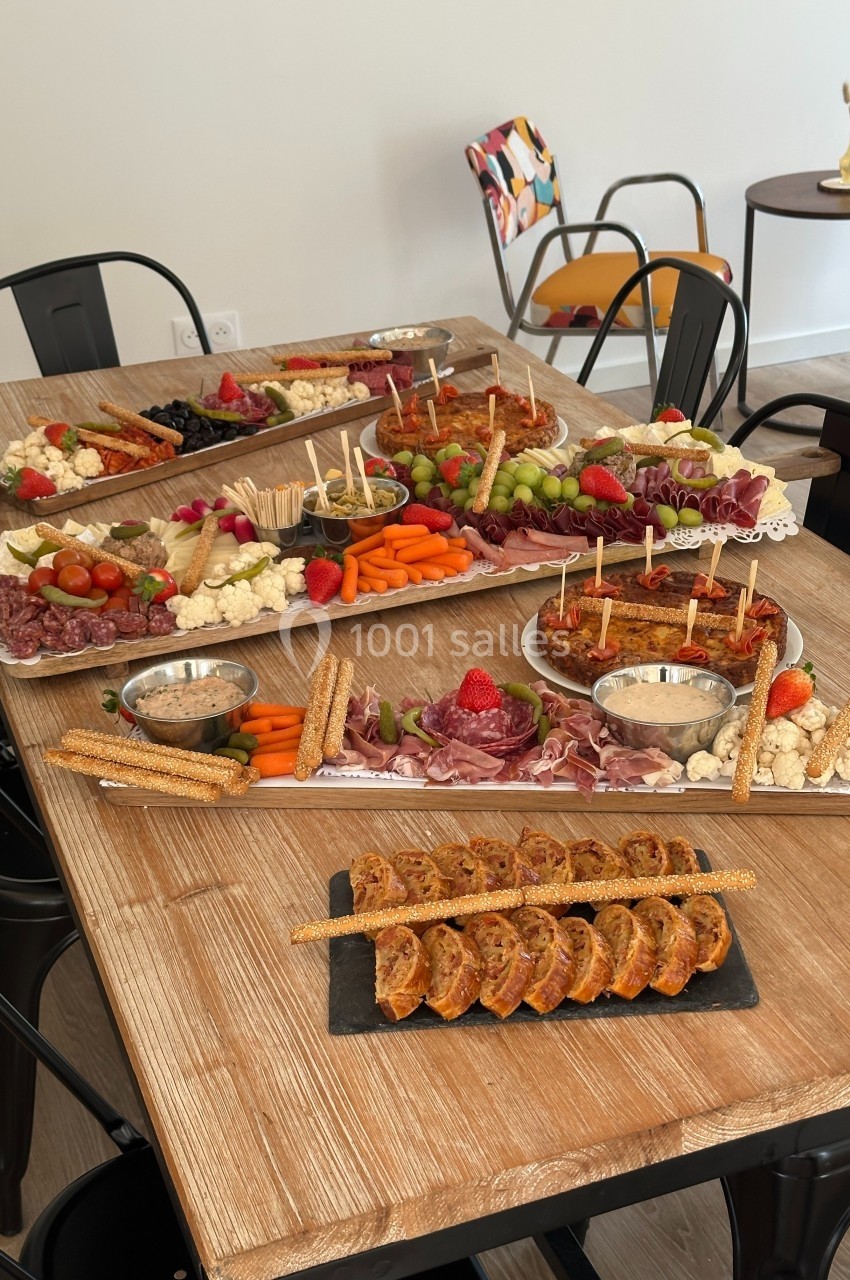 Plateau de table en bois avec assortiments de charcuteries, fromages, légumes, fruits et apéritifs variés.