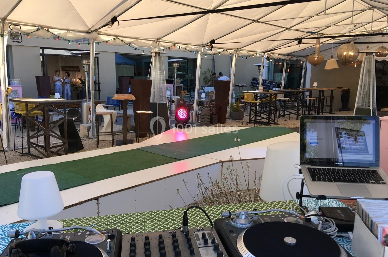 Terrasse couverte avec piste de danse, tables hautes, décoration lumineuse et équipement de DJ au premier plan.