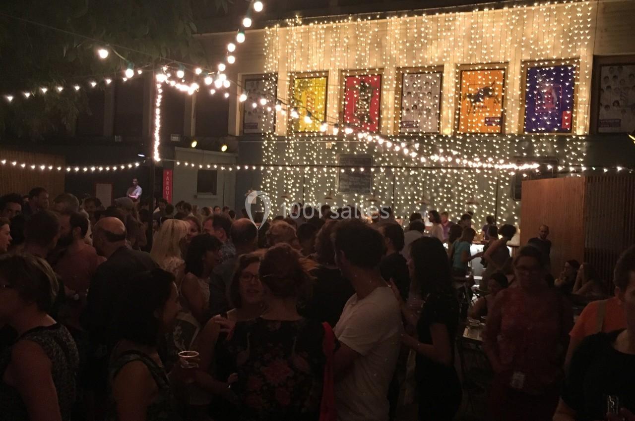 Foule rassemblée de nuit dans une cour éclairée par des guirlandes lumineuses, devant un bâtiment décoré.