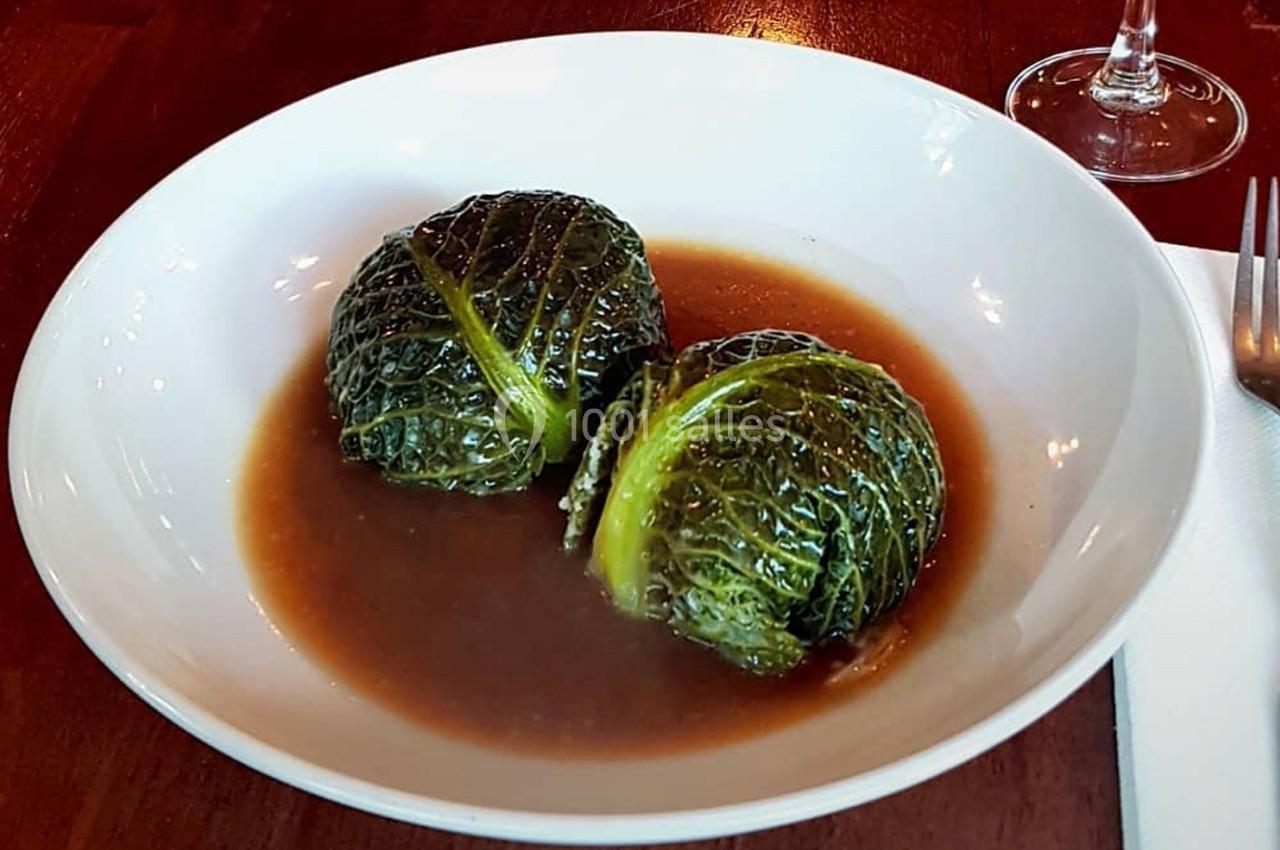 Deux choux farcis servis dans une assiette blanche avec une sauce brune, sur une table en bois.