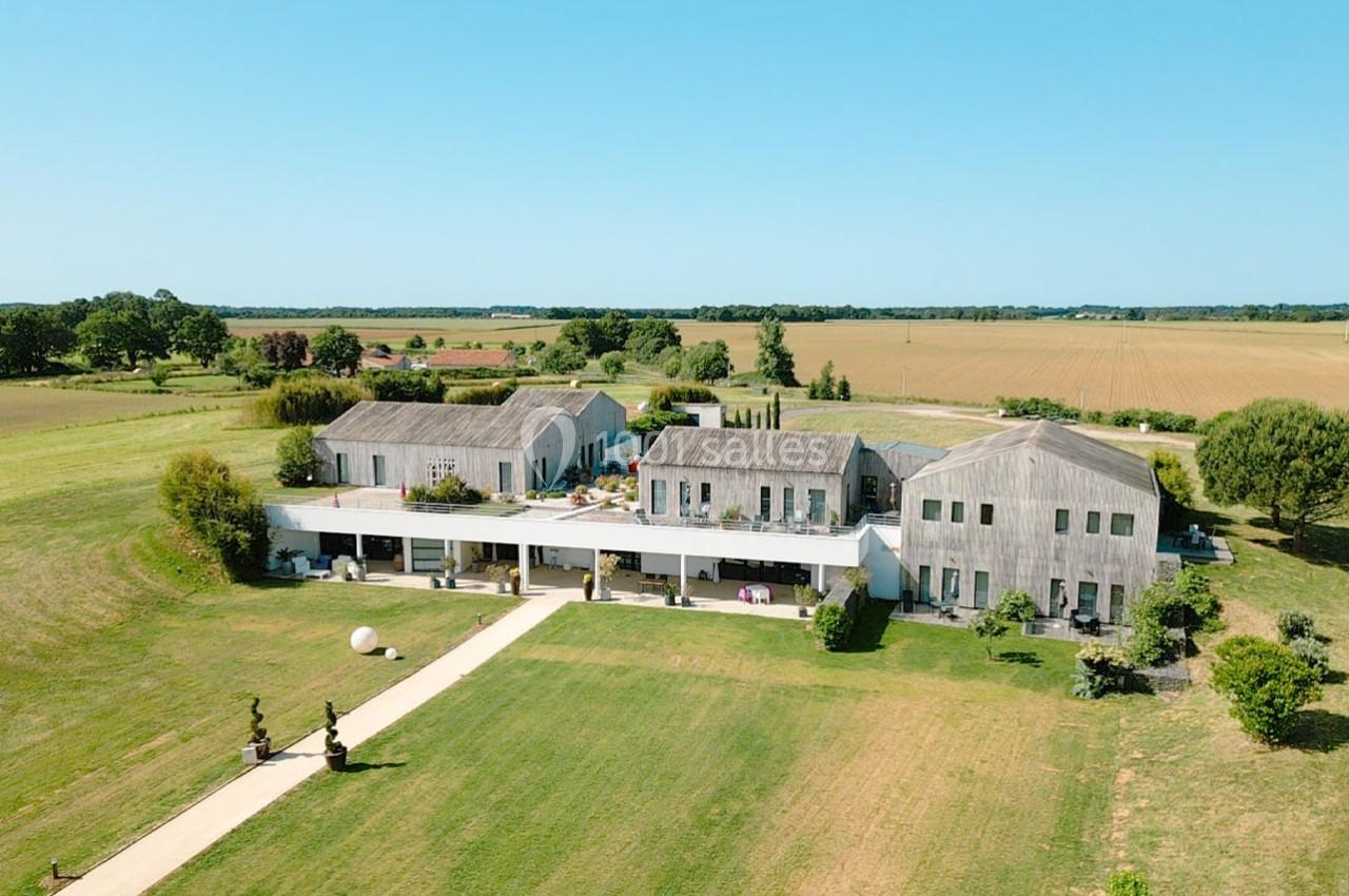 Vue aérienne d'un bâtiment moderne entouré de vastes champs et d'espaces verts sous un ciel dégagé.