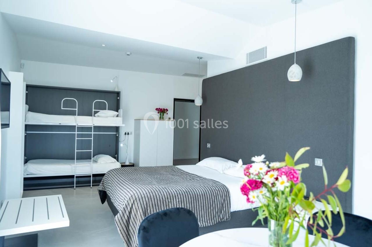 Chambre lumineuse avec un lit double, des lits superposés, une table avec fleurs et un décor moderne minimaliste.