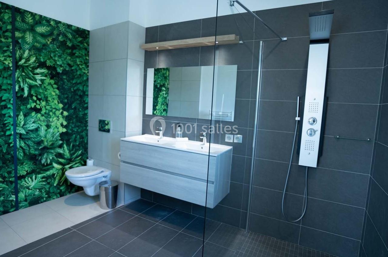 Salle de bain moderne avec douche à l'italienne, double vasque, toilettes et mur décoré de motifs végétaux.