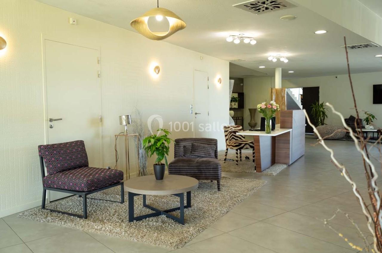 Salon moderne avec fauteuils, table basse, plantes et comptoir d'accueil dans un espace lumineux et épuré.