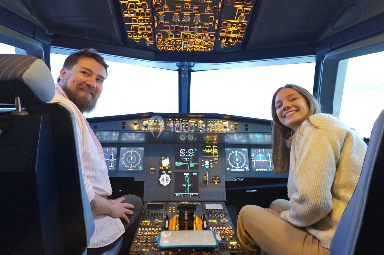Deux personnes assises dans le cockpit d'un avion, entourées de commandes et d'écrans lumineux.
