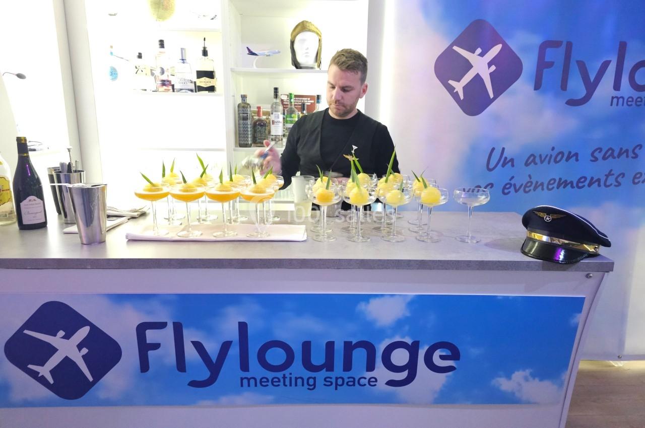 Un barman prépare des cocktails alignés sur un comptoir dans un espace événementiel décoré sur le thème de l'aviation.