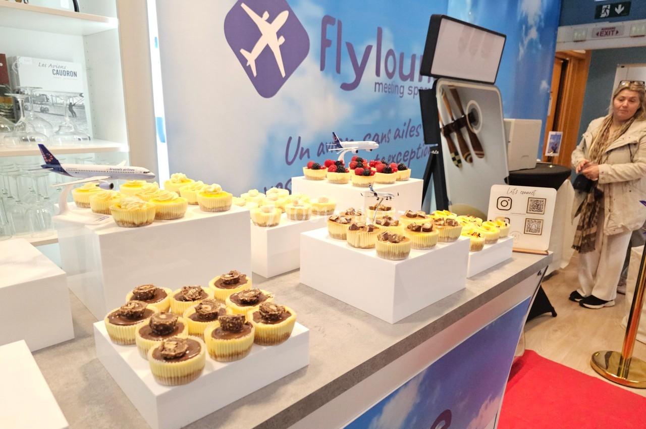Présentoir de cupcakes variés sur des socles blancs, dans un espace décoré sur le thème de l'aviation.