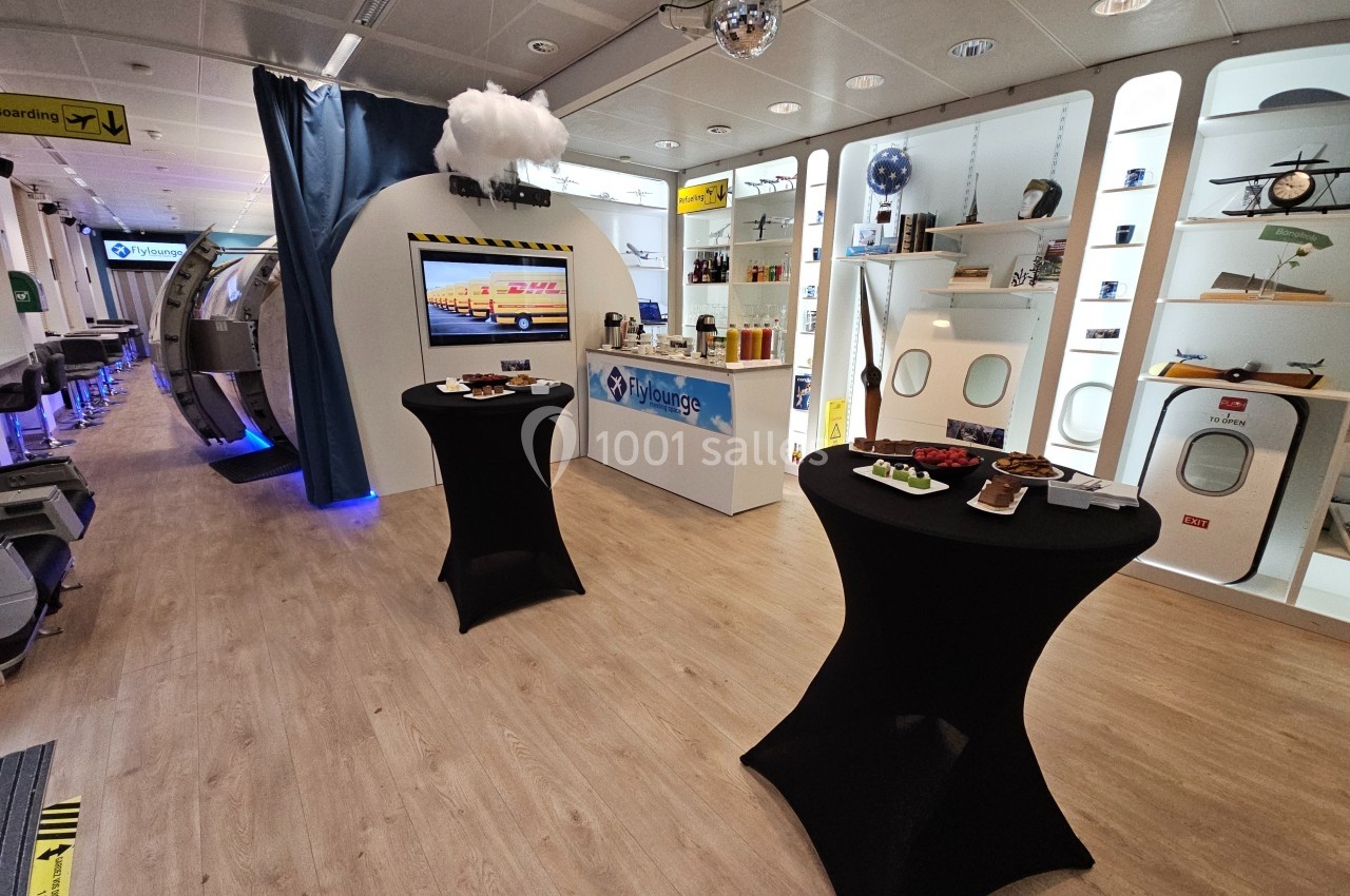 Salle aménagée sur le thème de l'aviation avec tables hautes, vitrines d'exposition et décorations aéronautiques.