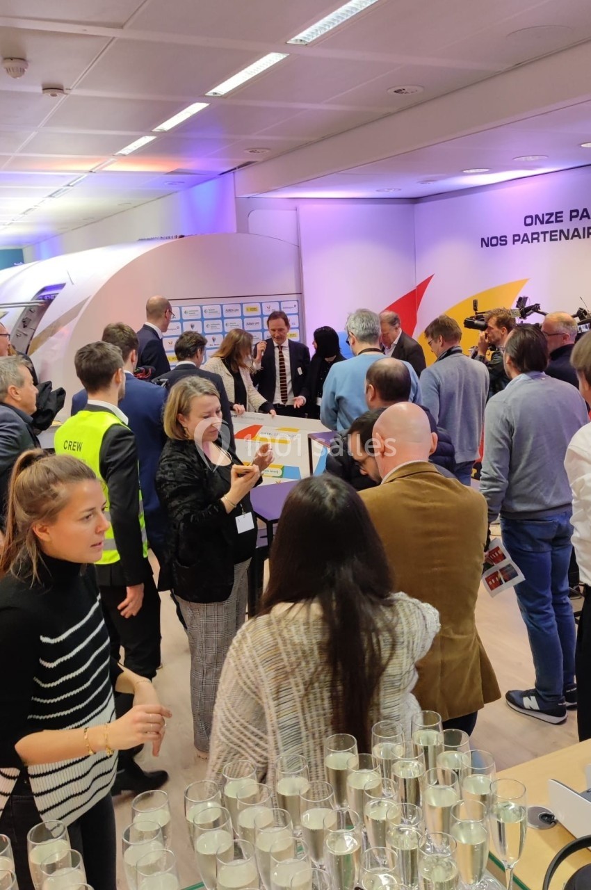 Groupe de personnes échangeant lors d'un événement dans une salle éclairée, avec des stands et des affiches en arrière-plan.