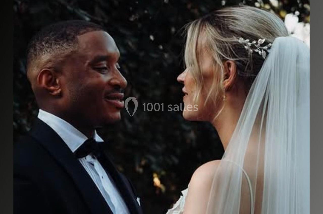 Un couple habillé en tenue de mariage se regarde face à face, avec un arrière-plan naturel et sombre.