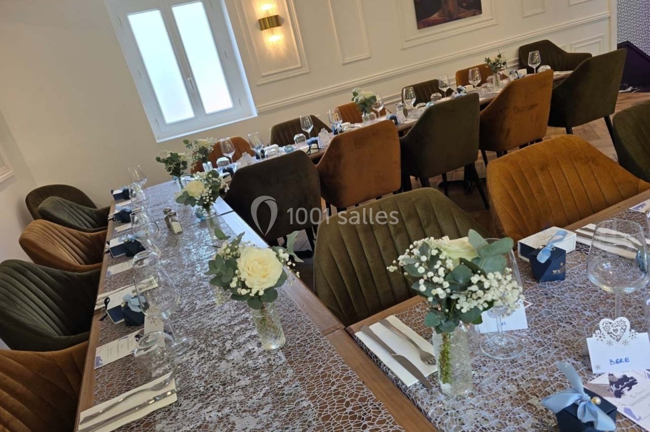 Salle de réception avec tables décorées de nappes en dentelle, fleurs blanches et couverts élégants.