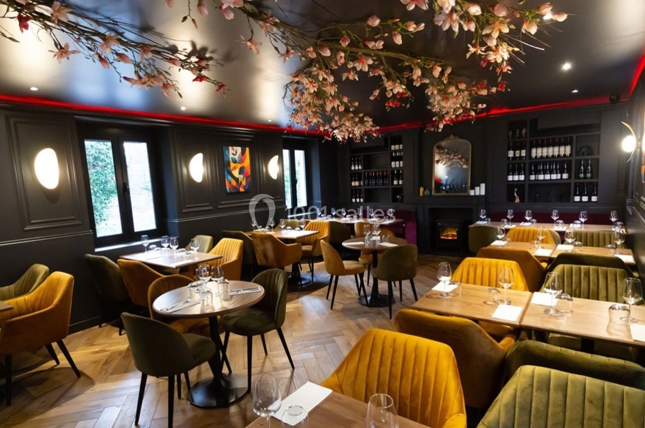 Salle de restaurant élégante avec tables en bois, chaises colorées et décoration florale suspendue au plafond.
