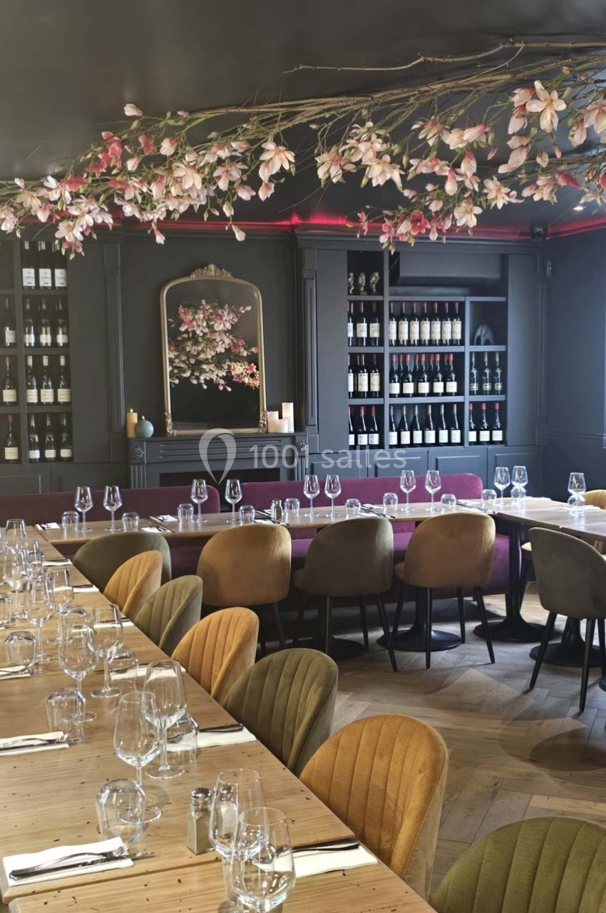 Salle de restaurant élégante avec tables dressées, chaises colorées et décoration florale suspendue.