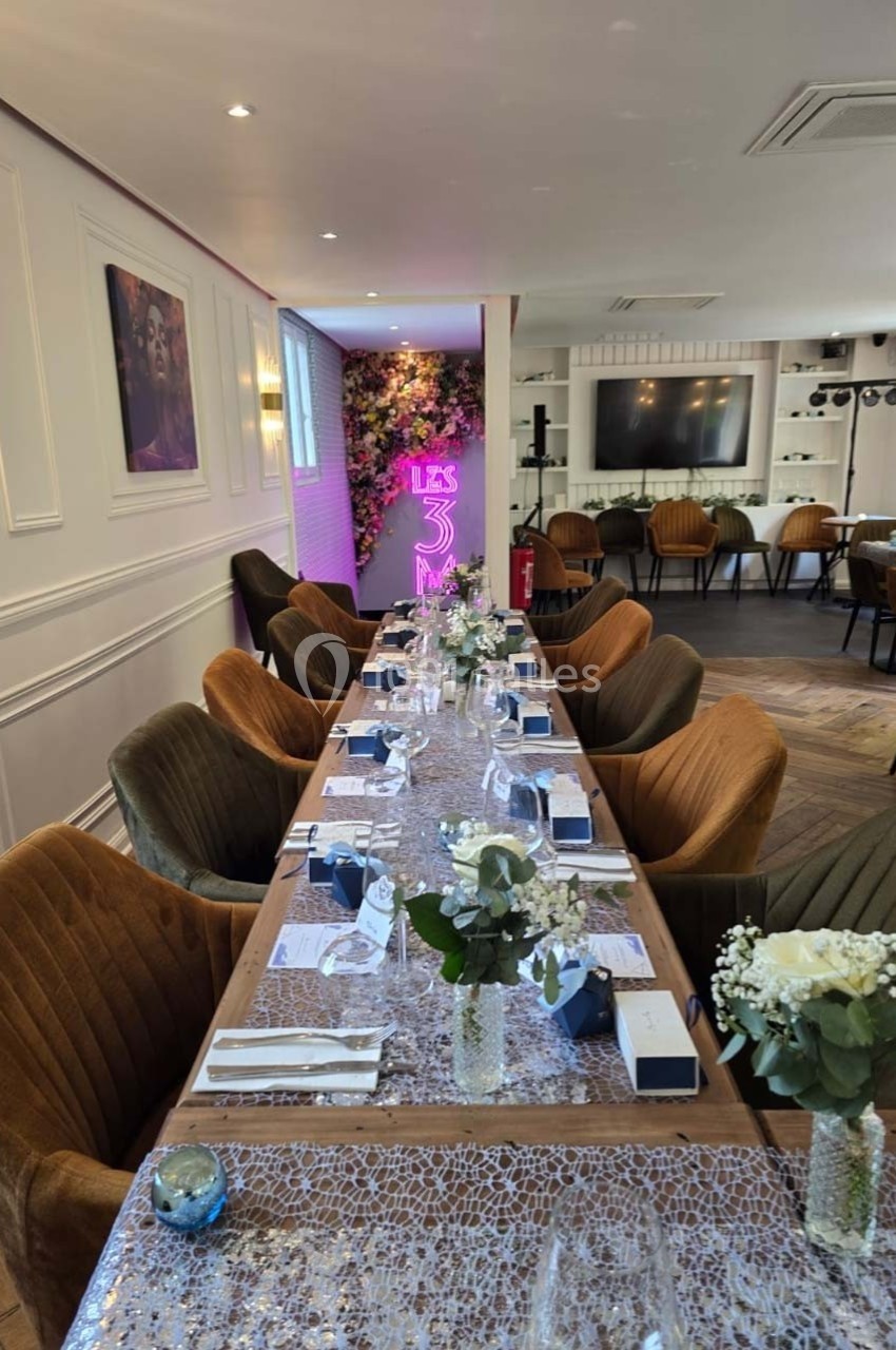 Salle de réception élégante avec une longue table dressée, décorée de fleurs et de cadeaux, éclairée par une lumière rose.