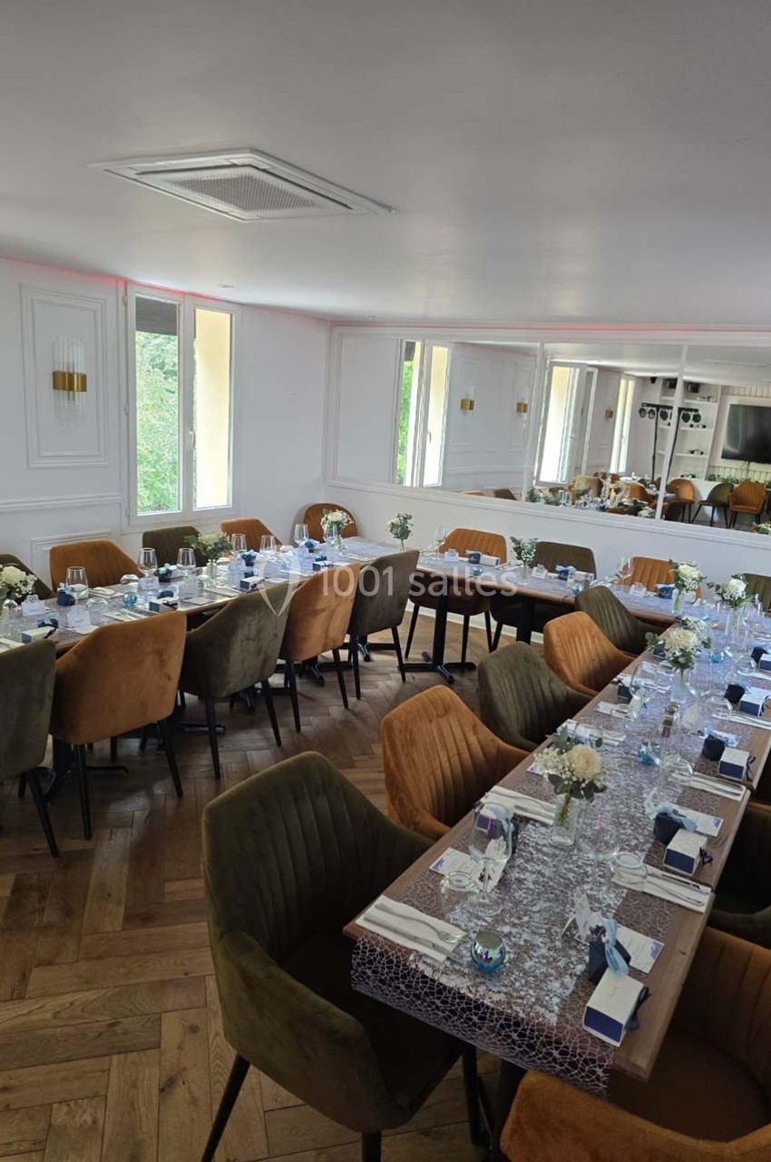 Salle de réception lumineuse avec deux longues tables dressées, décorées de fleurs et de vaisselle élégante.