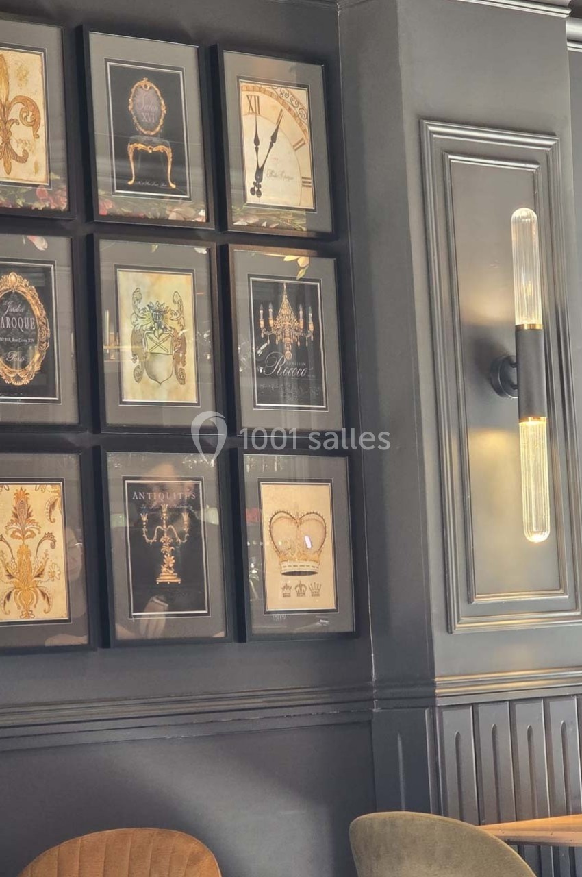 Mur décoré de cadres aux motifs variés, éclairé par une applique murale moderne, avec des fauteuils en premier plan.