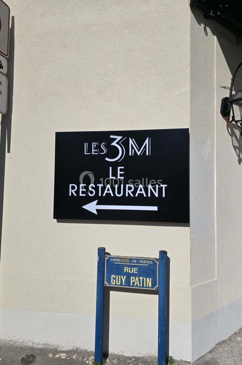 Panneau indiquant ’Les 3M Le Restaurant’ avec une flèche, situé à l'angle d'une rue nommée ’Rue Guy Patin’.