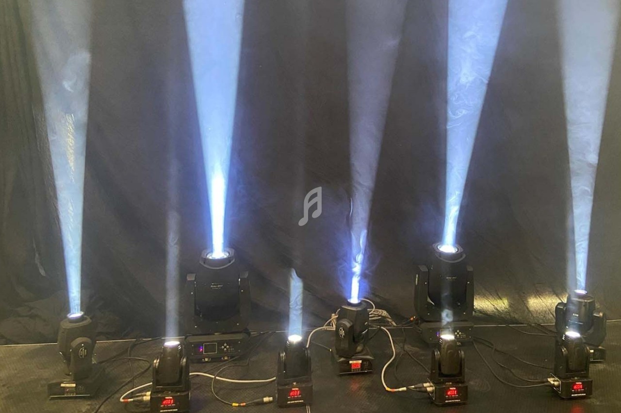 Projecteurs lumineux diffusant des faisceaux de lumière blanche sur un fond sombre, alignés sur une scène.