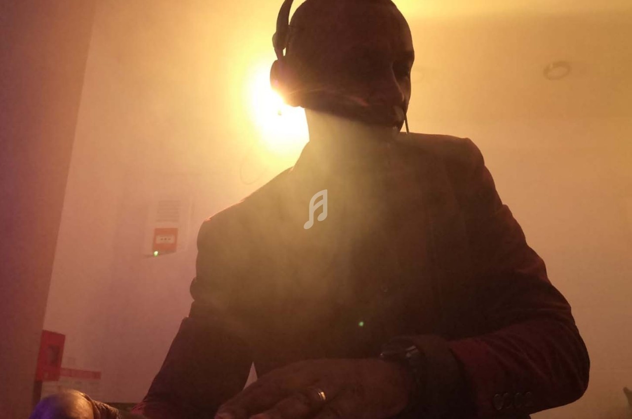 Un homme portant un casque-micro, éclairé par une lumière vive en arrière-plan, dans une ambiance enfumée.