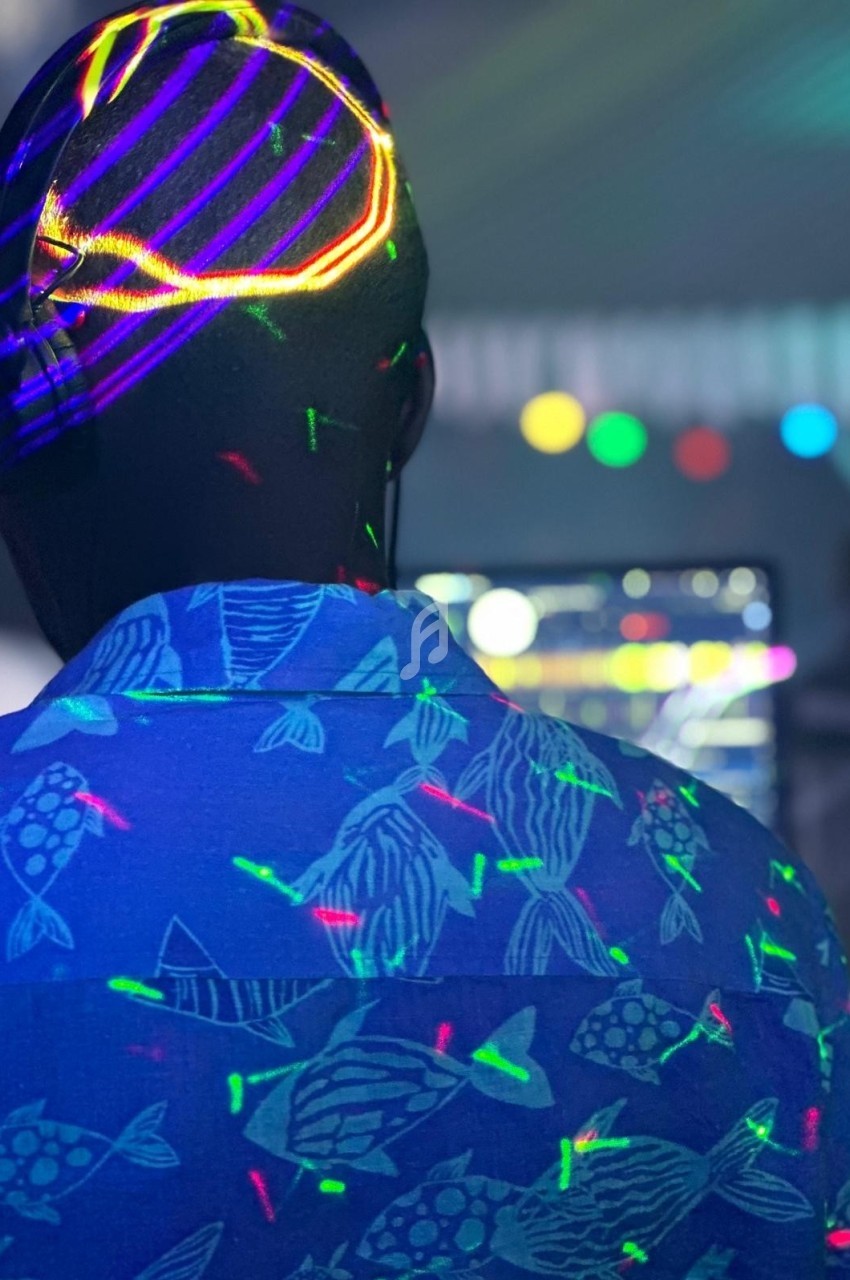 Personne de dos portant une chemise à motifs de poissons, éclairée par des lumières colorées dans une ambiance festive.