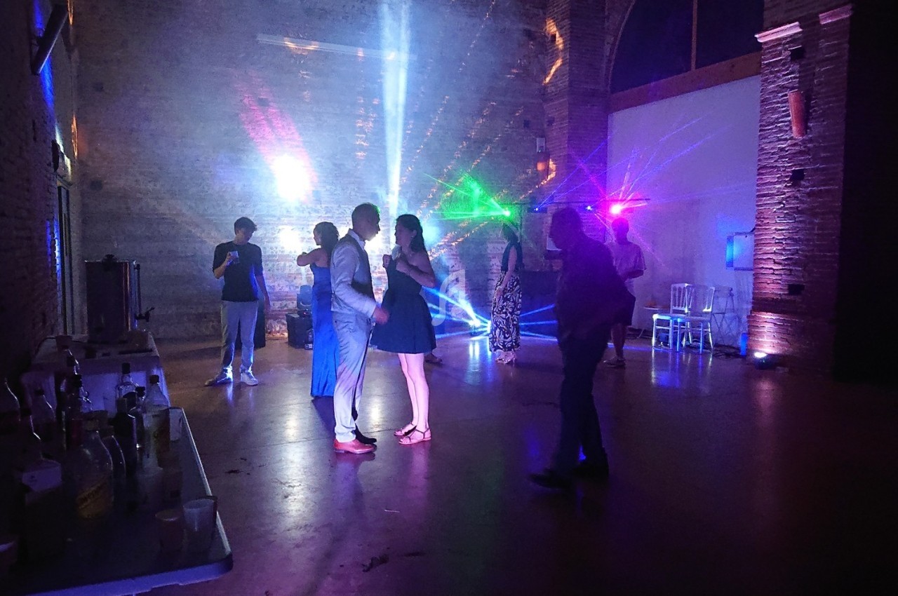 Des personnes dansent dans une salle faiblement éclairée avec des jeux de lumière colorés et des tables en arrière-plan.