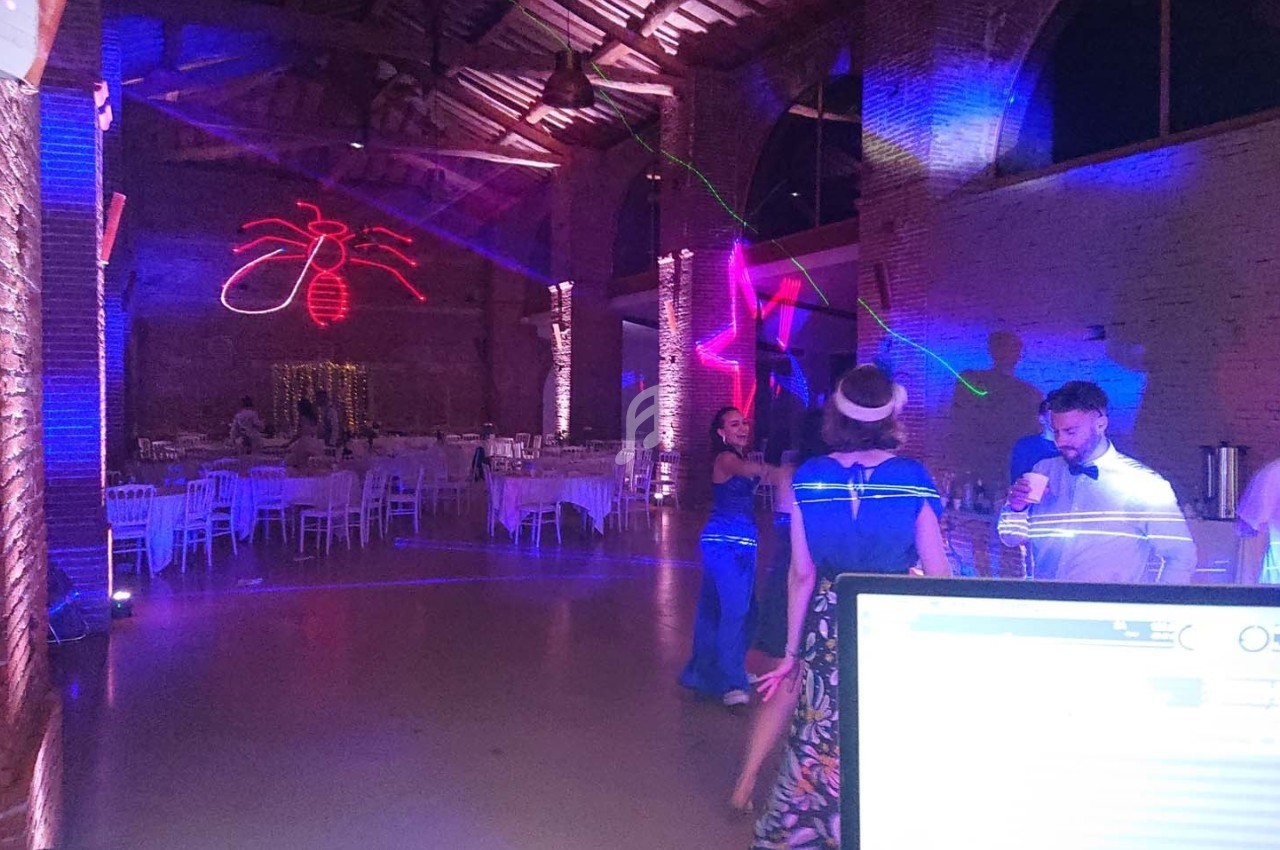 Salle de réception avec éclairages colorés, invités dansant et tables dressées en arrière-plan.