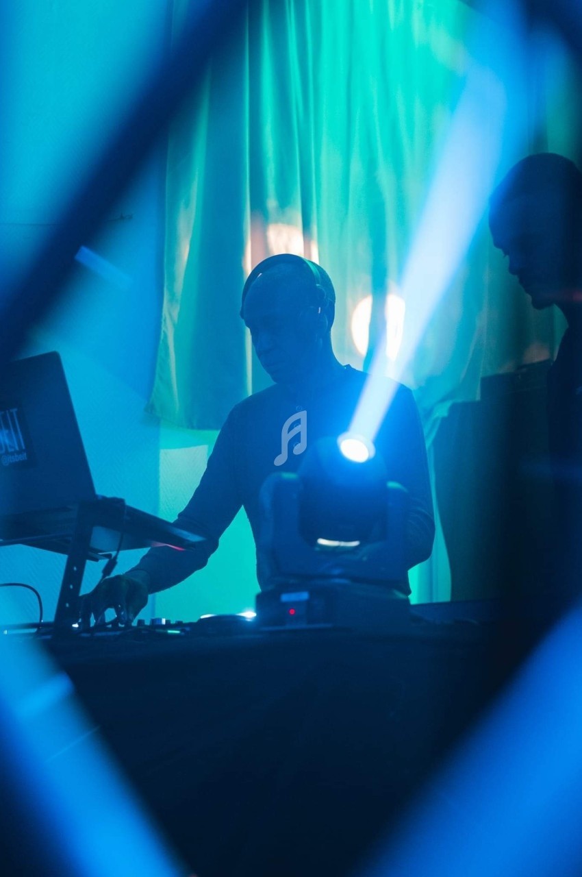 Un DJ mixant sur une scène éclairée par des lumières bleues, avec un projecteur lumineux au premier plan.
