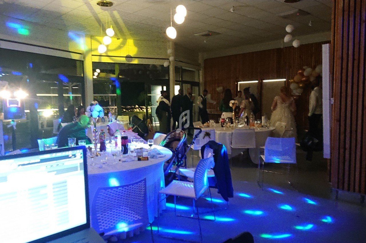 Salle de réception illuminée avec des invités, tables dressées et ambiance festive en soirée.