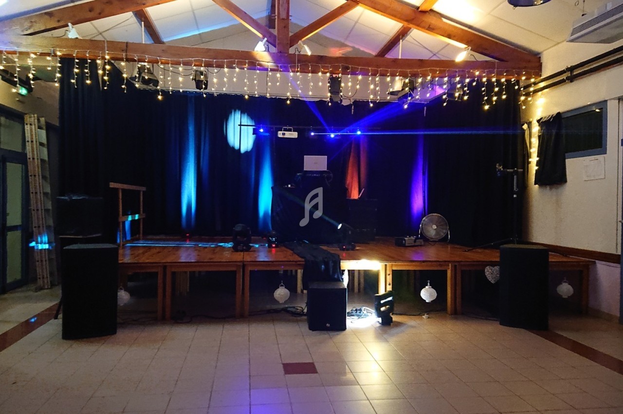 Scène décorée avec guirlandes lumineuses, éclairages colorés et équipements audio dans une salle intérieure.