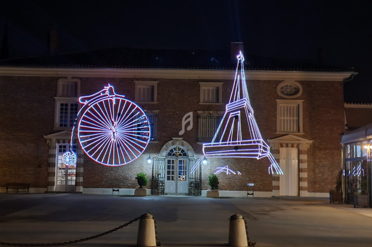Façade d'un bâtiment éclairée la nuit avec des décorations lumineuses représentant un grand-bi et la tour Eiffel.