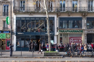 Façade d'un théâtre et d'une parapharmacie sur une avenue parisienne, avec des passants et des vélos stationnés.