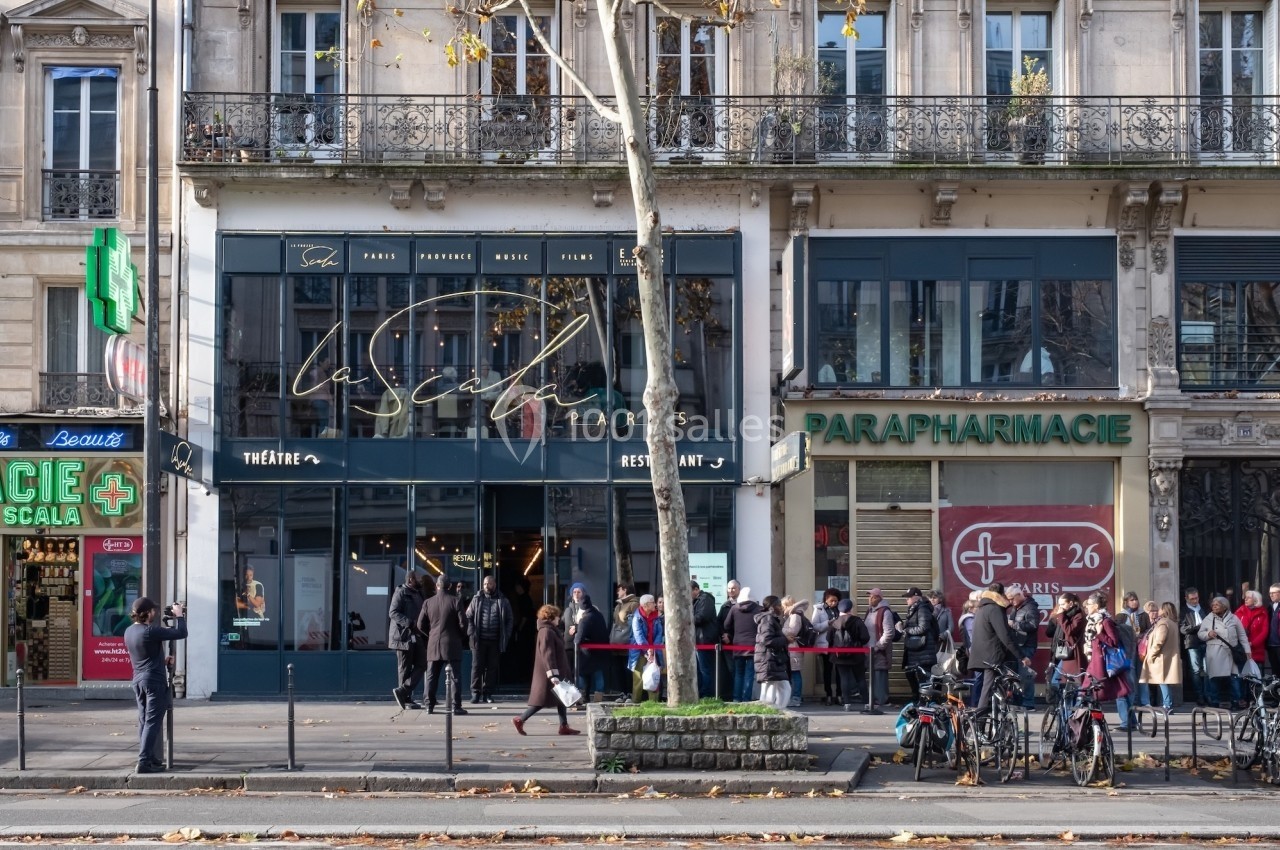 Façade d'un théâtre et d'une parapharmacie sur une avenue parisienne, avec des passants et des vélos stationnés.