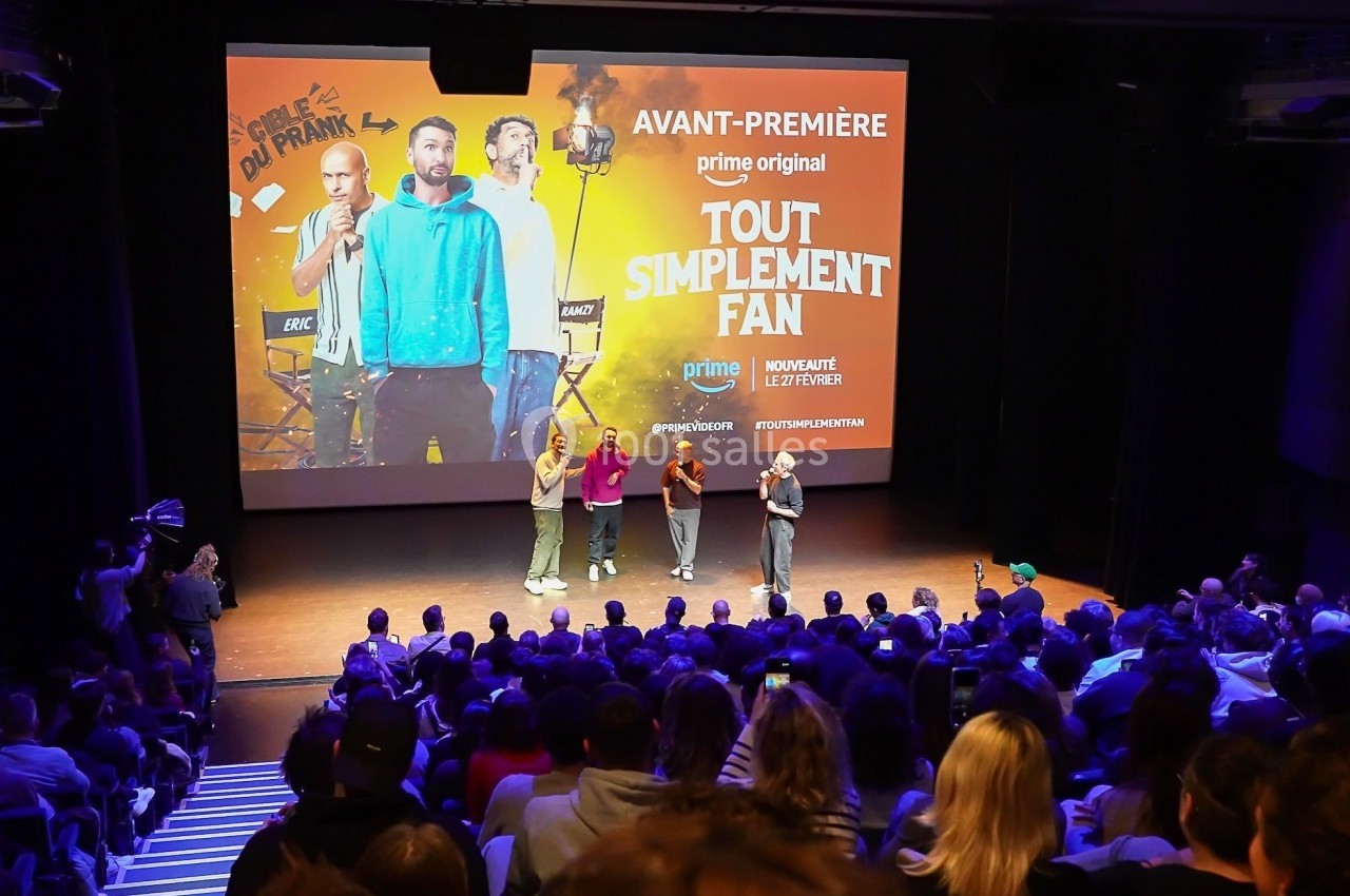 Quatre personnes sur scène devant un public, lors d'une avant-première avec une affiche projetée en arrière-plan.
