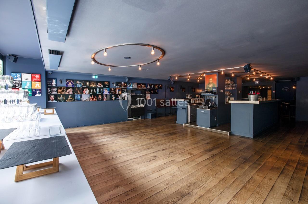 Salle moderne avec parquet en bois, bar à droite, étagères décorées au fond et table avec verres à gauche.
