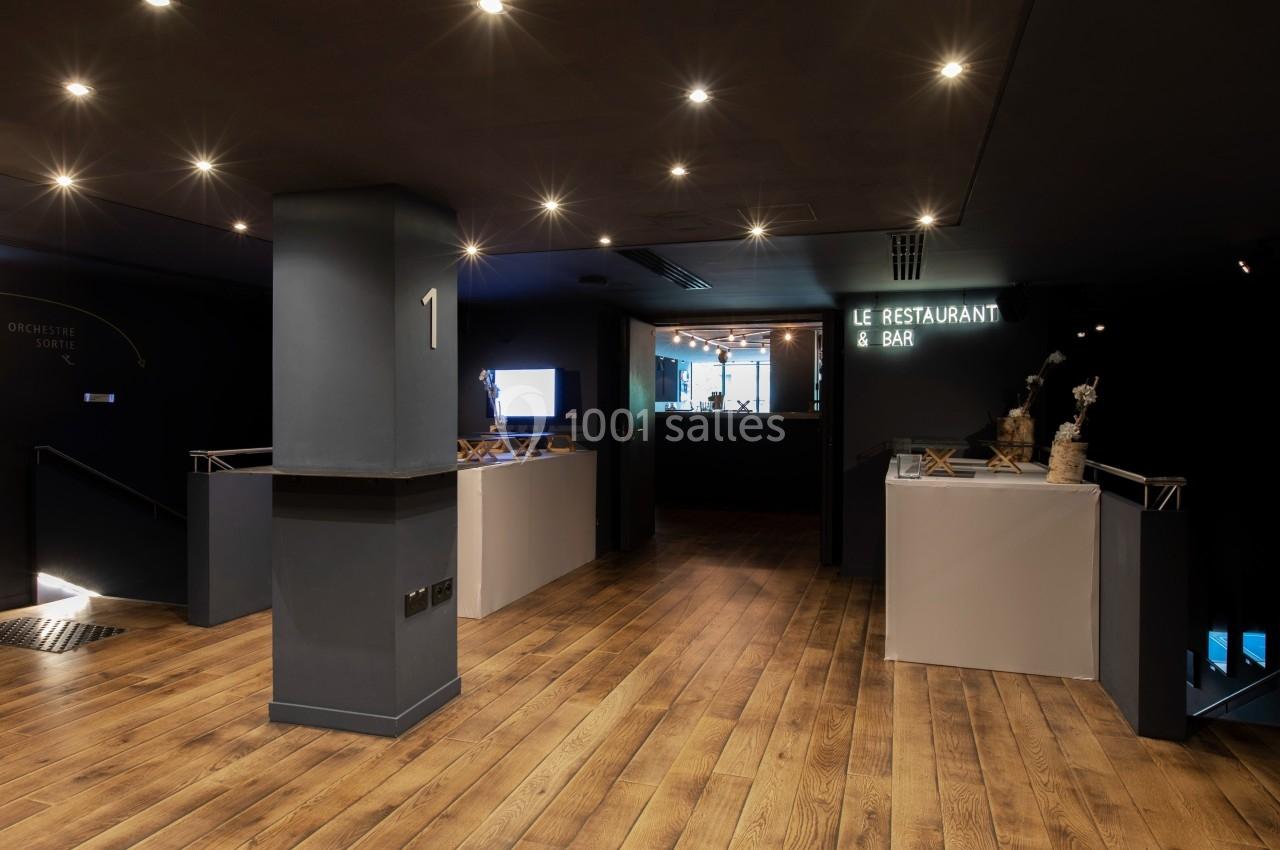 Hall d'entrée sombre avec sol en bois, éclairage tamisé, signalisation pour un restaurant et bar au fond.