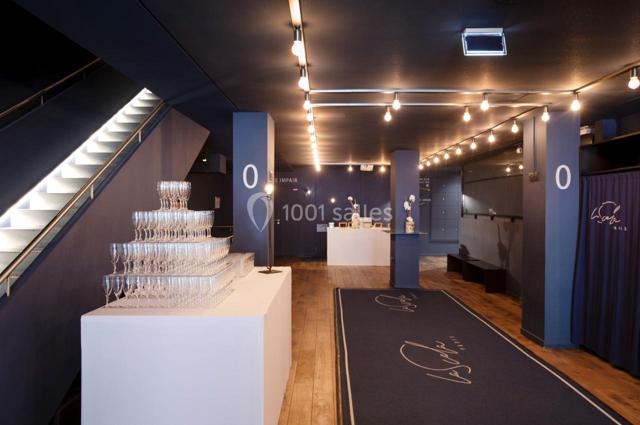 Hall d'entrée élégant avec moquette bleue, comptoir d'accueil, présentoir de coupes et éclairage chaleureux.