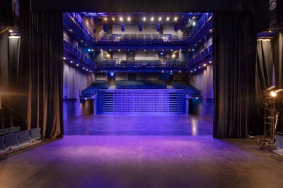 Salle lumineuse avec parquet, grandes baies vitrées donnant sur une rue urbaine, et comptoirs blancs alignés.