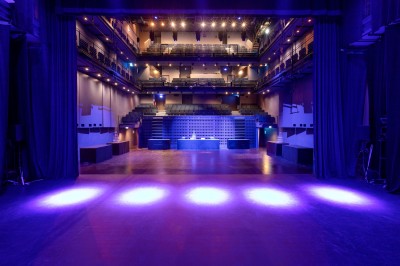 Salle lumineuse avec parquet, grandes baies vitrées donnant sur une rue urbaine, et comptoirs blancs alignés.