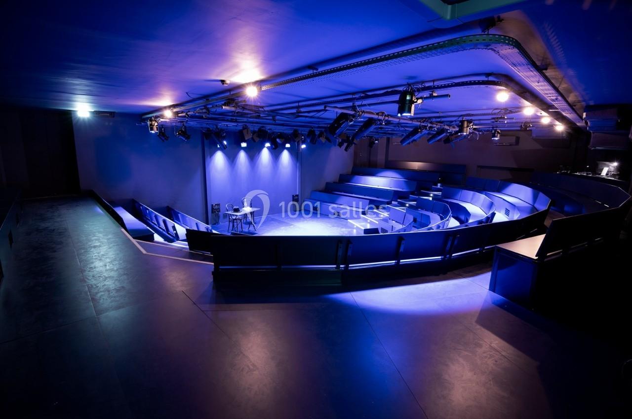 Salle de spectacle moderne avec gradins vides, éclairée par des projecteurs bleus et violets.