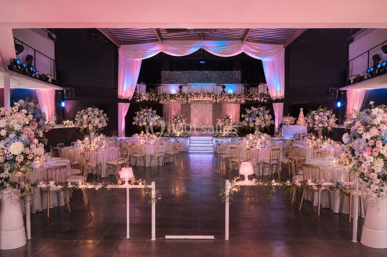 Salle de réception décorée avec des fleurs blanches et roses, tables dressées et éclairage tamisé.