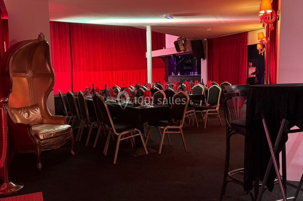 Salle décorée avec des rideaux rouges, tables dressées avec chaises noires et dorées, ambiance tamisée.