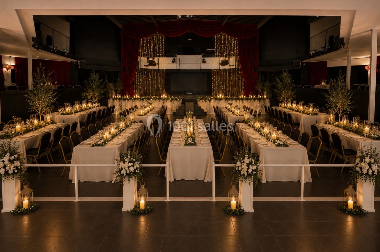 Salle de réception décorée avec des tables alignées, bougies, guirlandes lumineuses et arrangements floraux élégants.