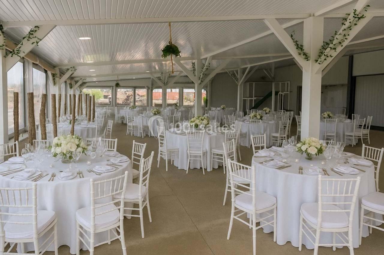 Salle de réception lumineuse avec tables rondes décorées de nappes blanches, chaises assorties et arrangements floraux.