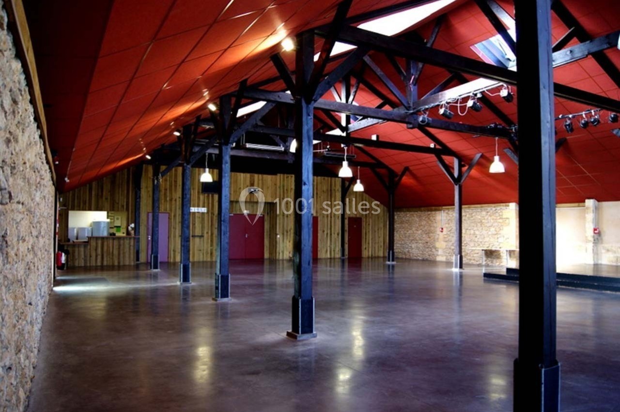 Salle spacieuse avec charpente en bois, murs en pierre et bois, sol en béton poli, éclairage suspendu.