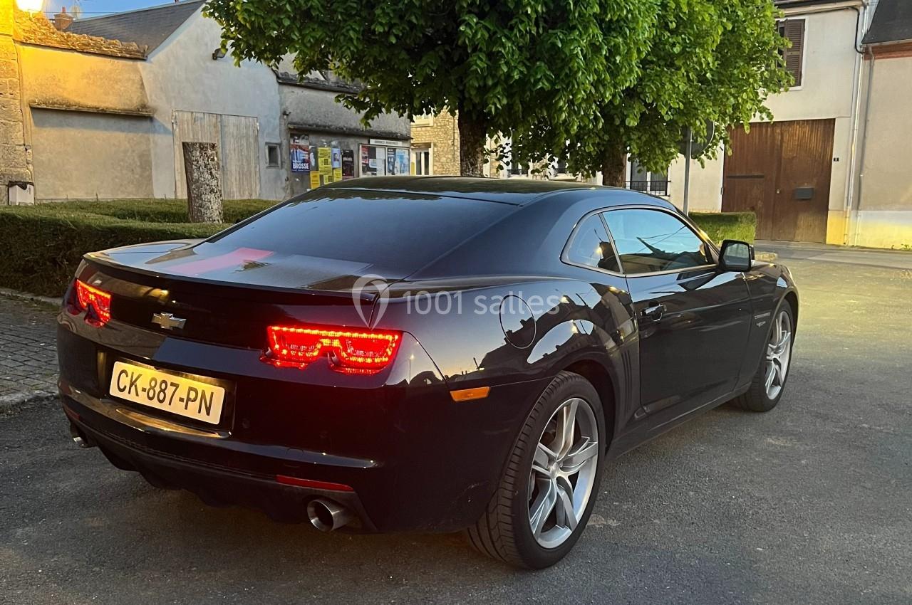 Voiture noire sportive garée sur une place pavée, éclairée par une lumière de fin de journée.
