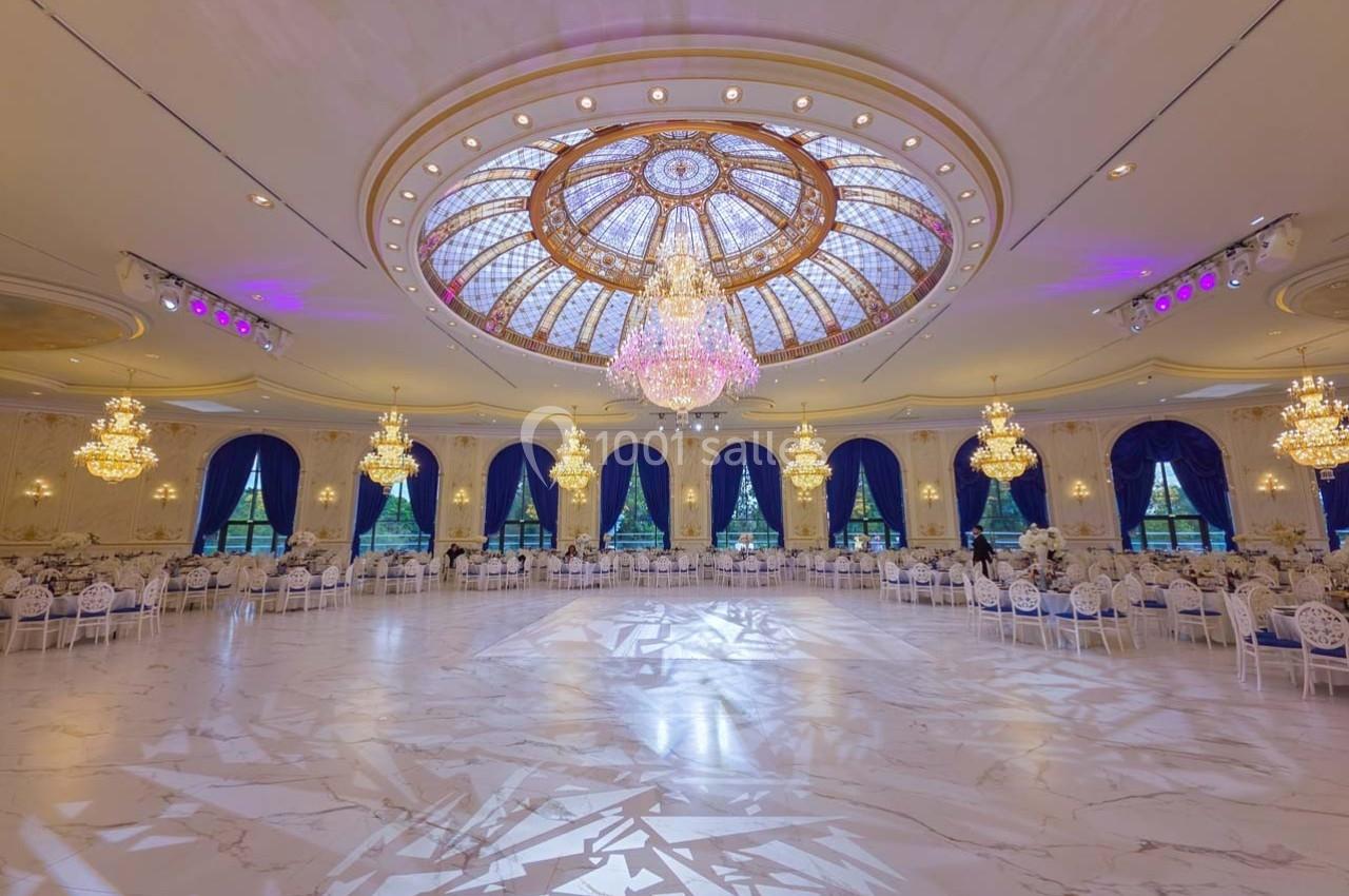 Salle de réception élégante avec un plafond orné de vitraux, lustres imposants et sol en marbre clair.