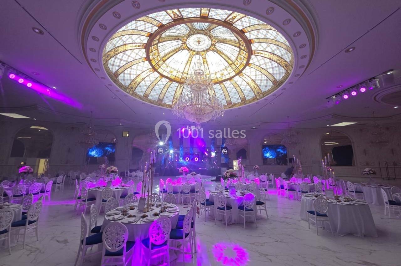 Salle de réception élégante avec tables dressées, éclairage violet et grand dôme en vitrail au plafond.