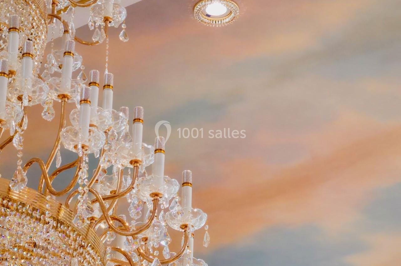 Lustre en cristal doré suspendu sous un plafond peint avec des nuances pastel de bleu et de rose.